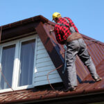 roofer builder worker spraying paint on metal sheet roof